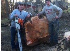 Two workers standing by a large cut trunk section and chainsaw
